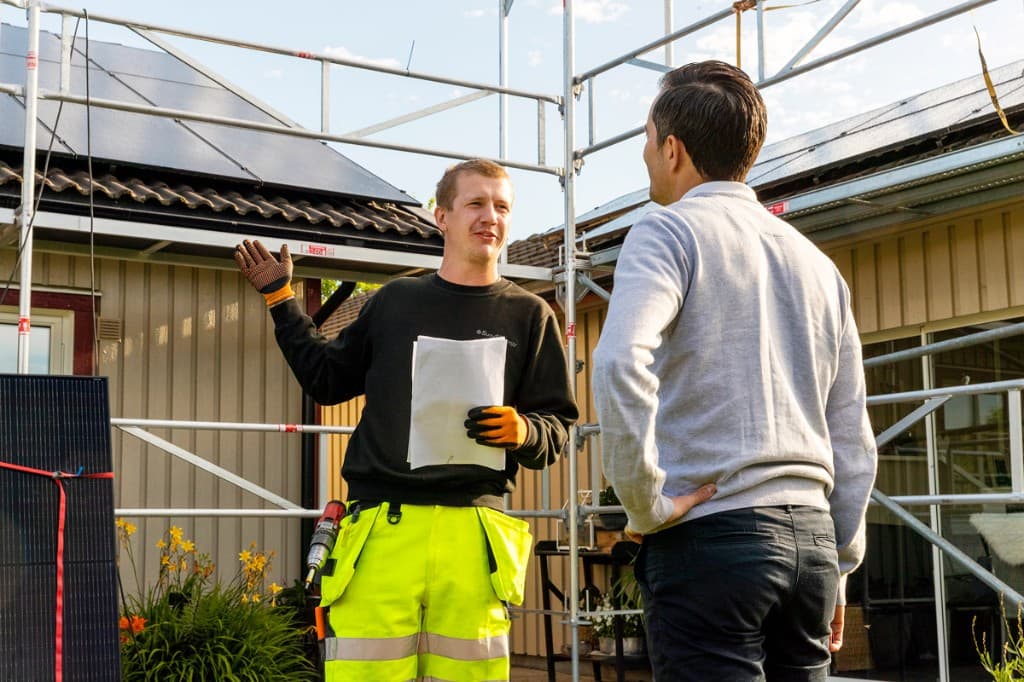 Installatör och kund i samtal framför hus med solceller på taket